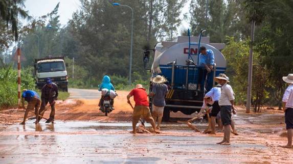 Công nhân quét dọn lớp bùn đỏ tràn qua đoạn đường Phan Thiết - La Gi  - Ảnh: Hữu Thành